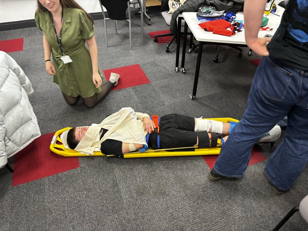 Student practicing spinal immobilization on yellow stretcher during Give It A Go event