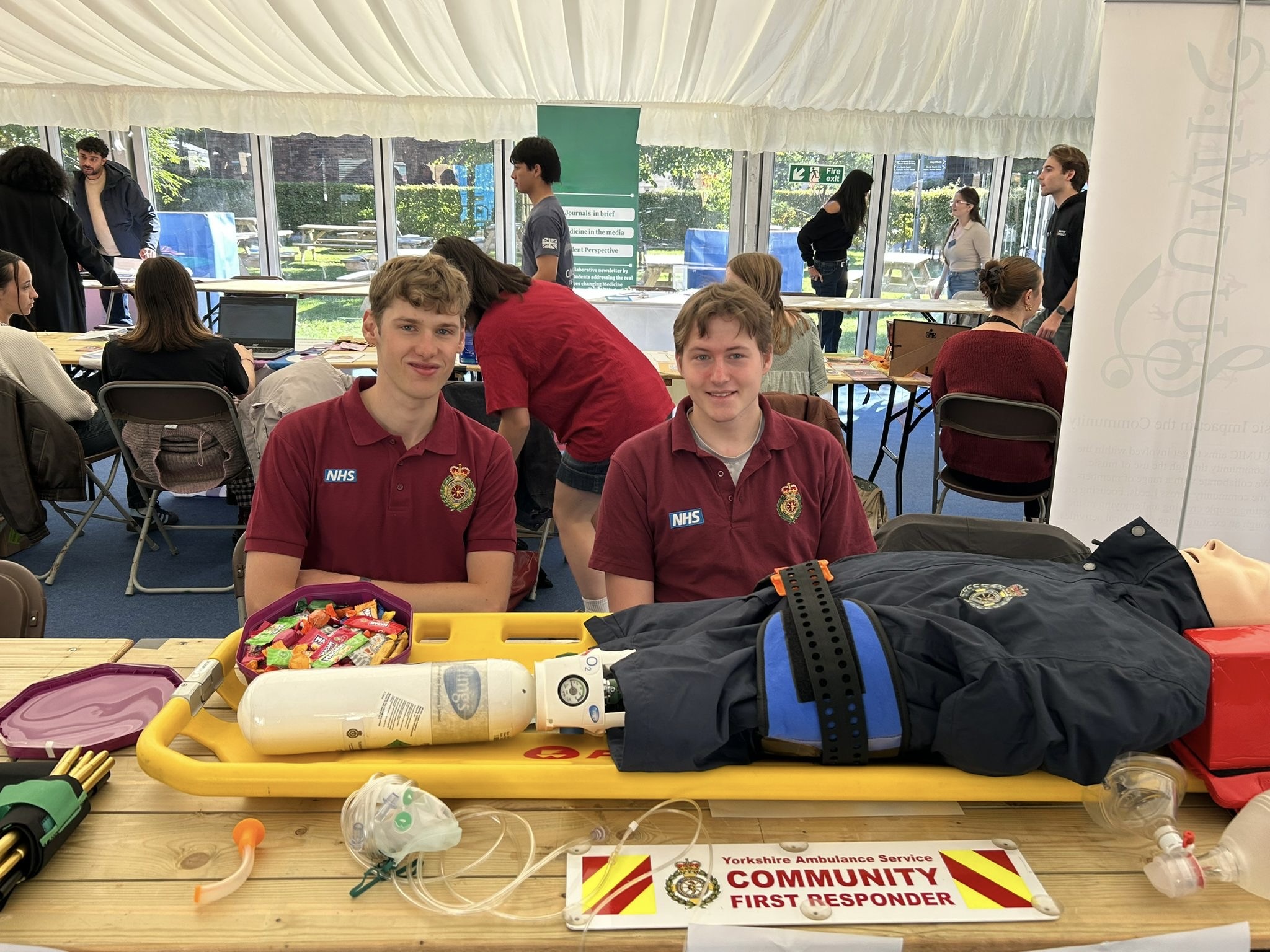 Cam and Rory at the LSCFR stall with full equipment display including CPR mannequin, oxygen, and CFR banner